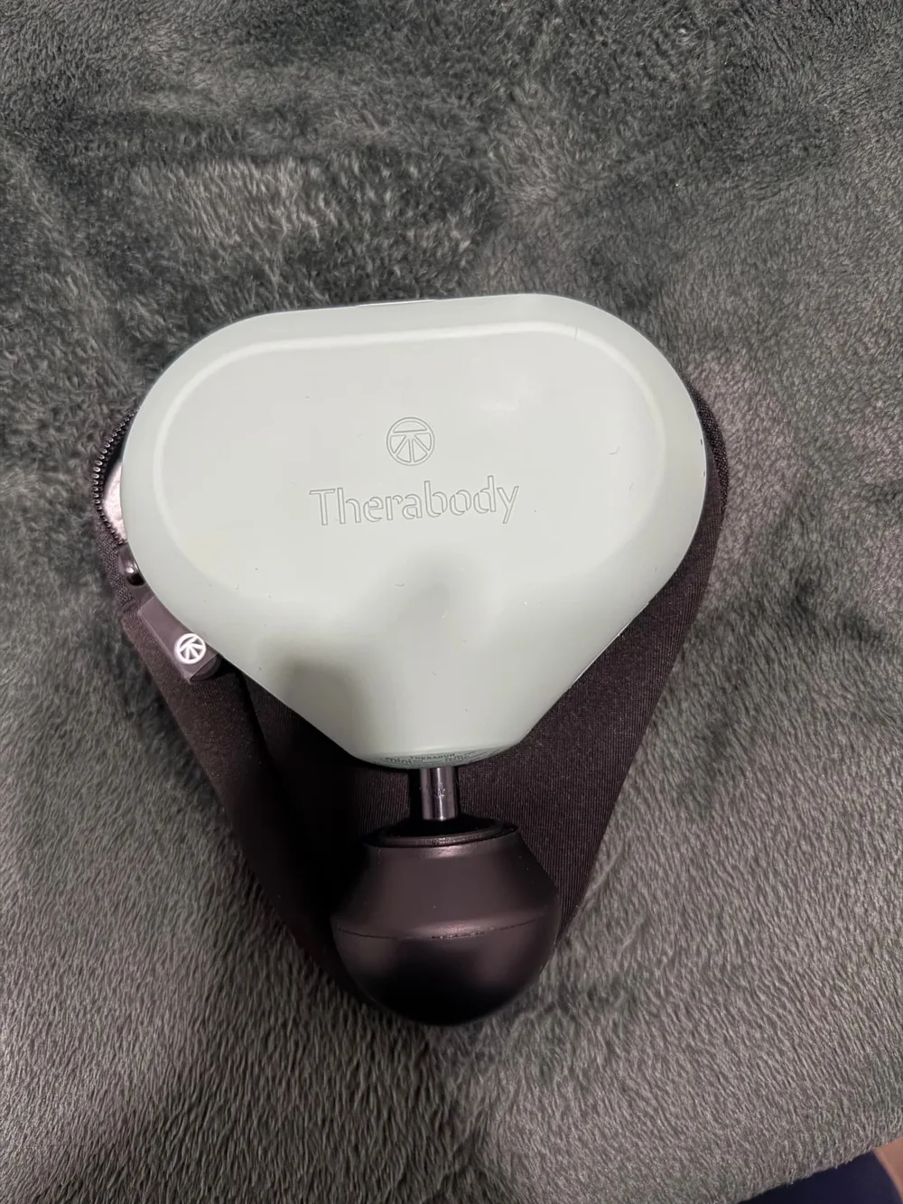 Therabody percussion device resting in its case on a soft grey blanket